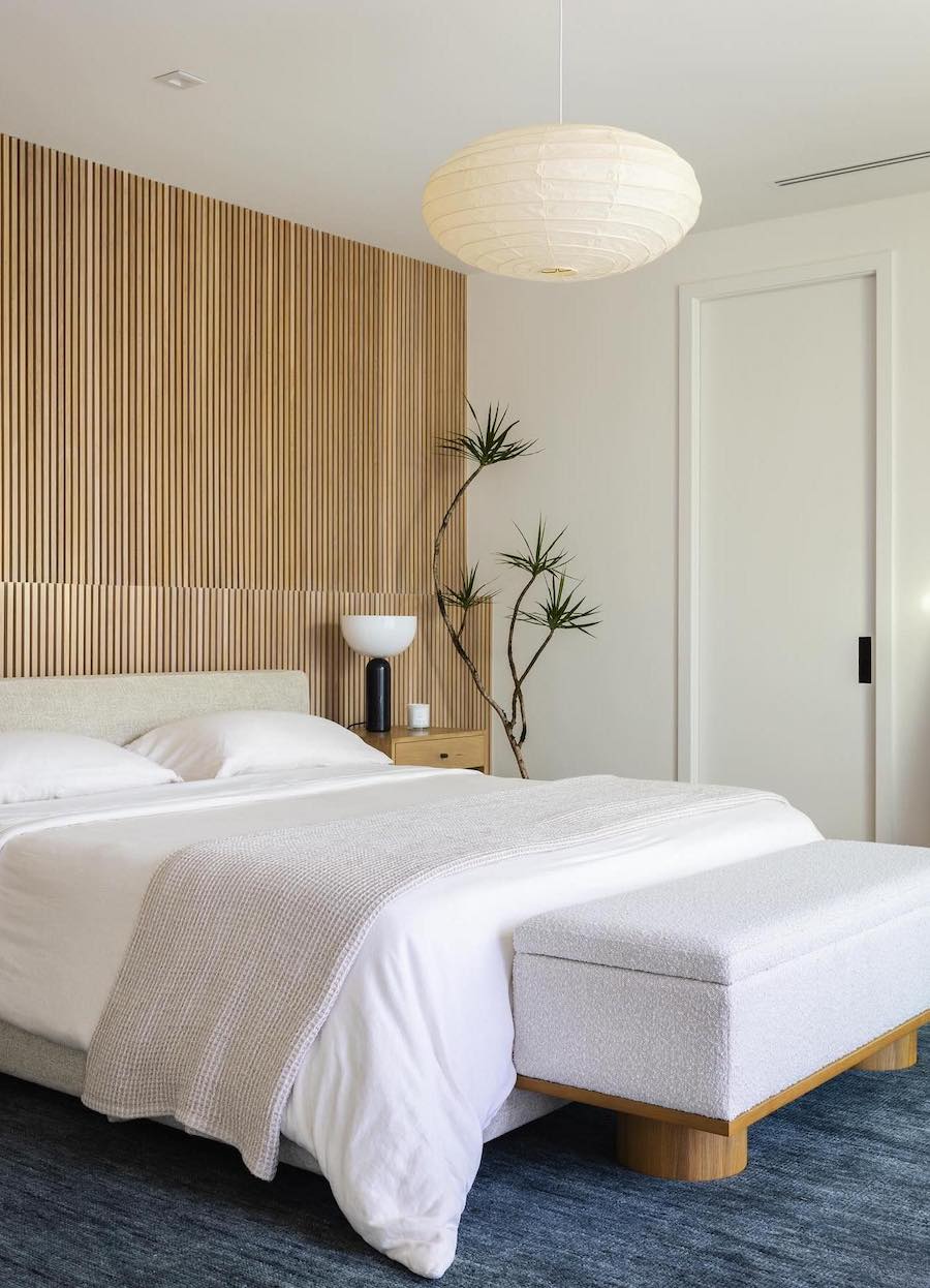 a minimalist bedroom featuring a bamboo accent wall, ivory linens, and unique plants