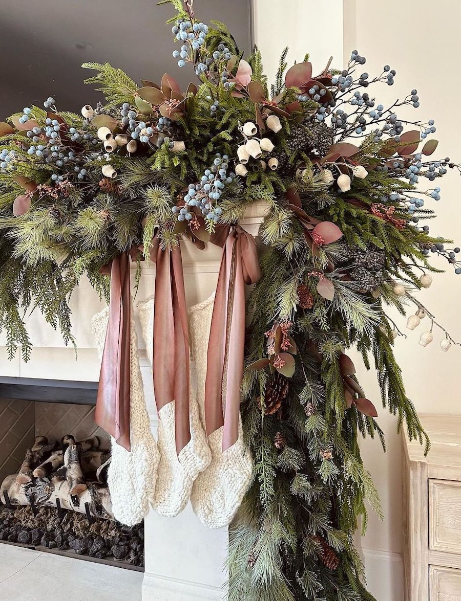 a christmas mantle with pine garland featuring pinecones, pink ribbons, white flowers, and blueberries