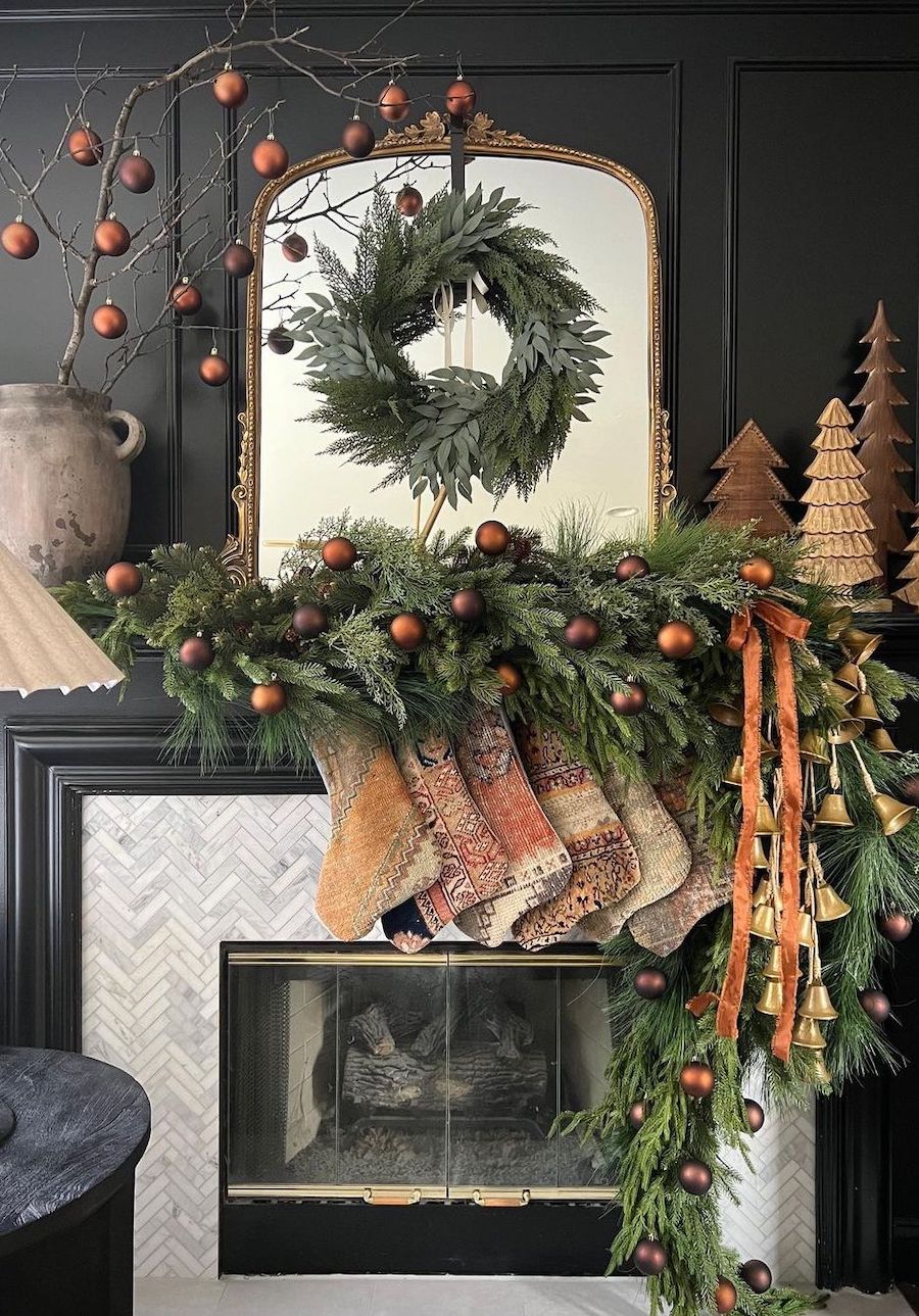 a christmas mantle with green garland and bronze ornaments and christmas trees