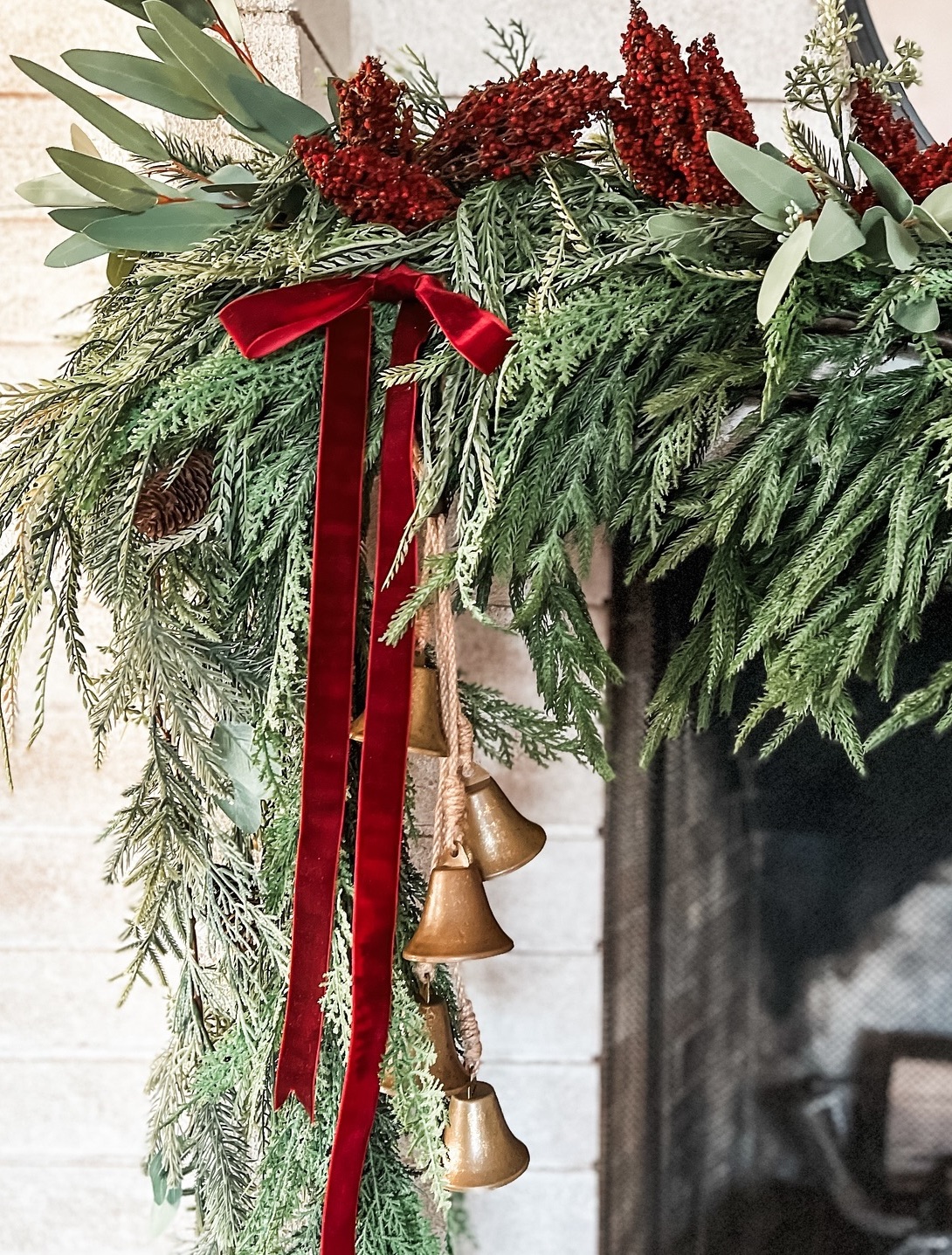 a christmas mantle decorated with pine, berries, and red velvet ribbons