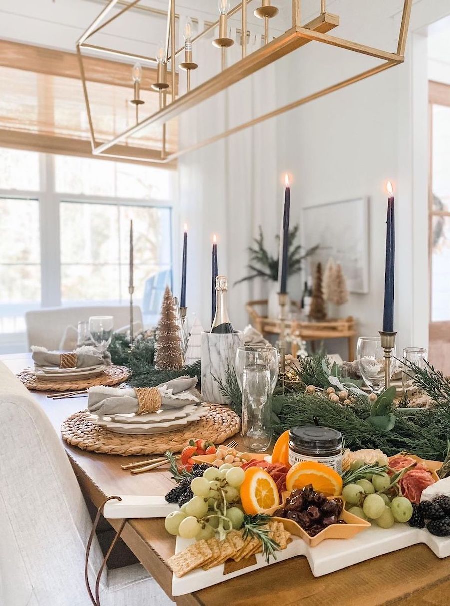 christmas table decorations featuring charcuterie boards, pine, tall candles, and trees