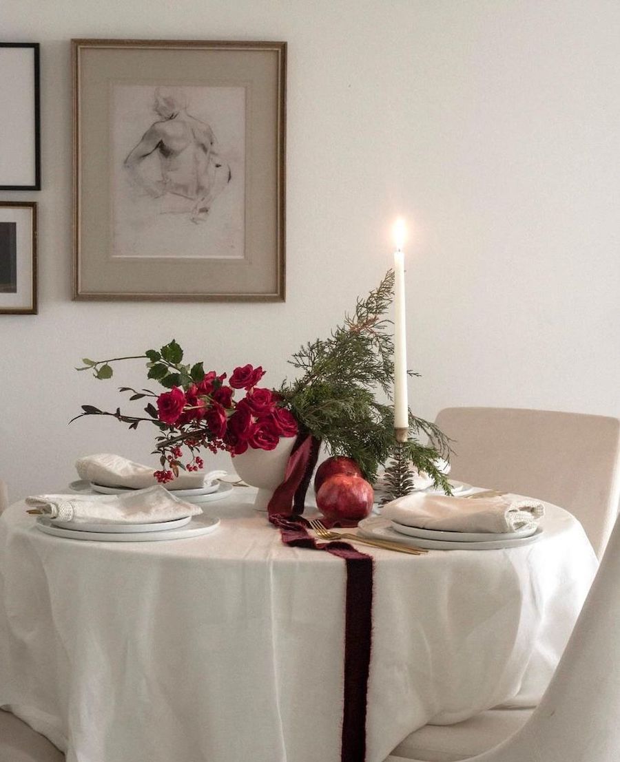 christmas table decorations featuring white linens, pomegranates, red roses, pine, and tall candles