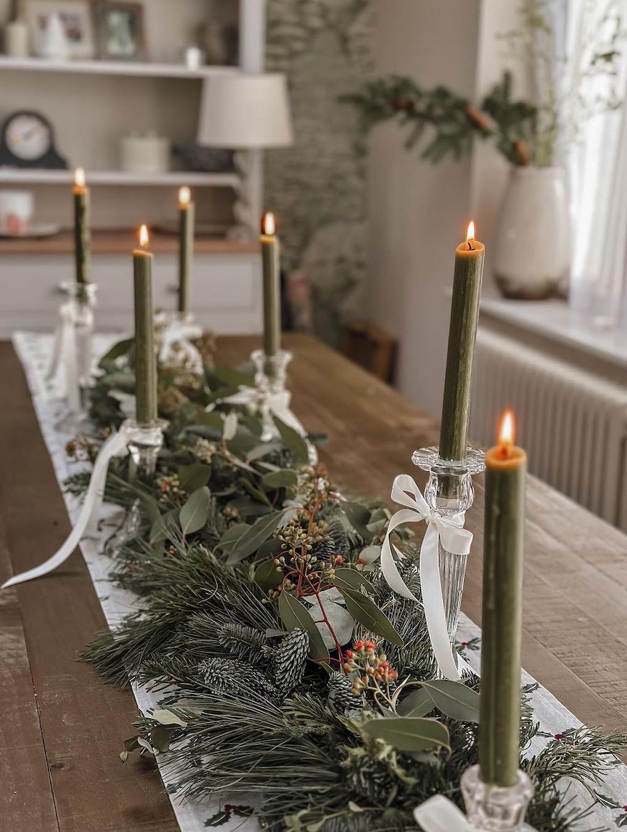 christmas table decorations featuring pine, eucalyptus, pinecones, green candles, and white ribbons