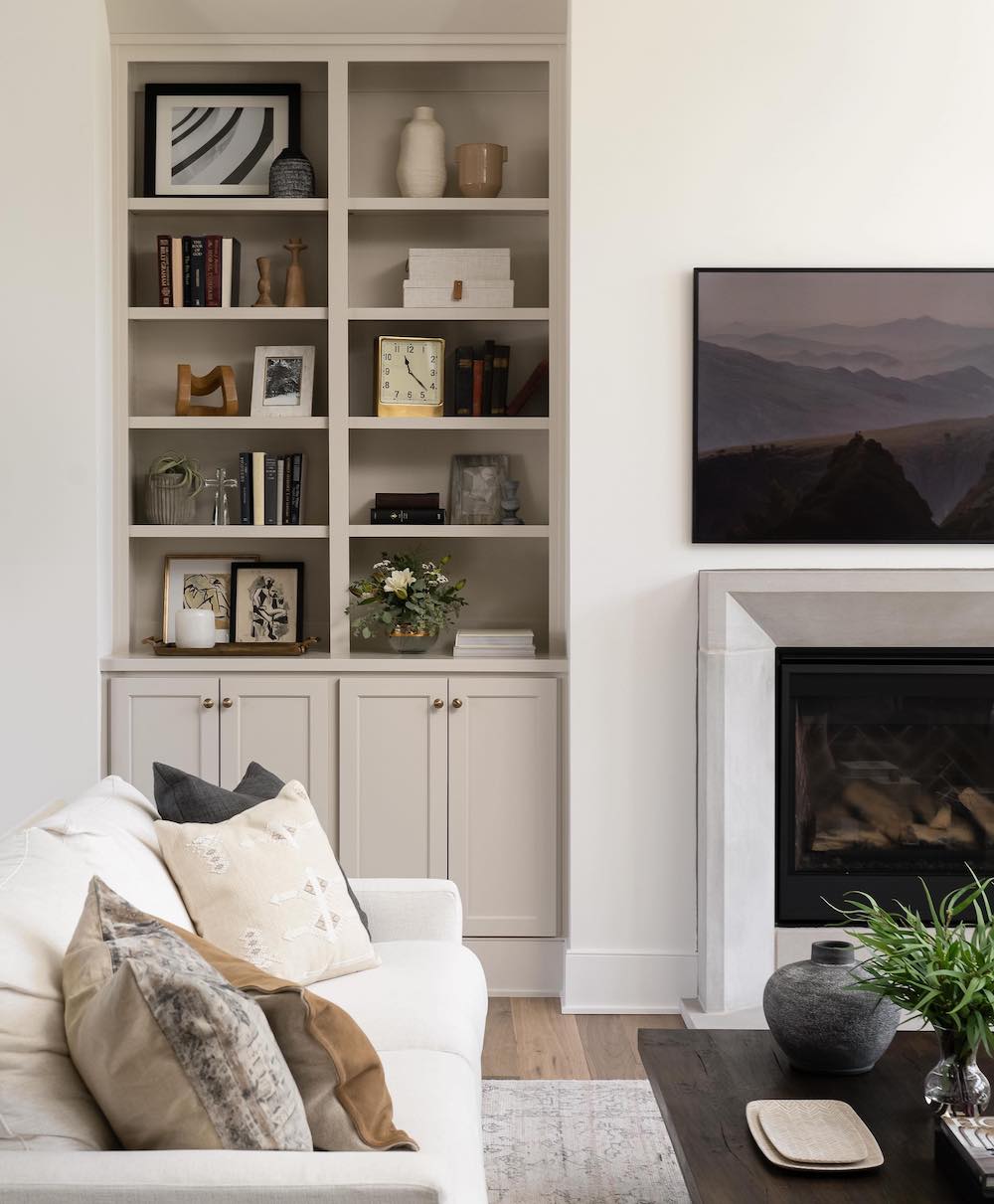 a modern neutral room featuring built-in shelves and cabinets next to the fireplace