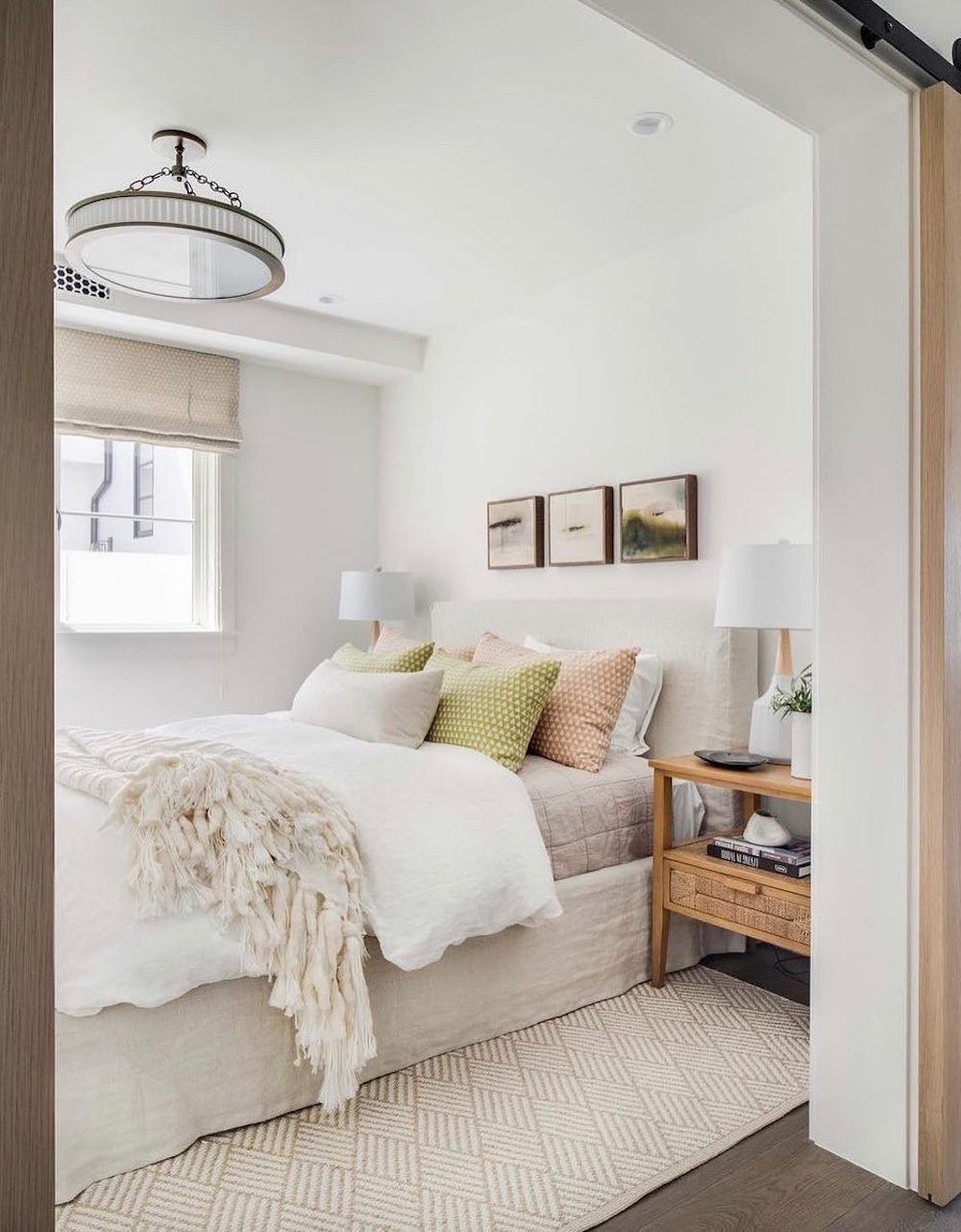 a small bedroom with ivory bedding with pops of green and pink and modern decor