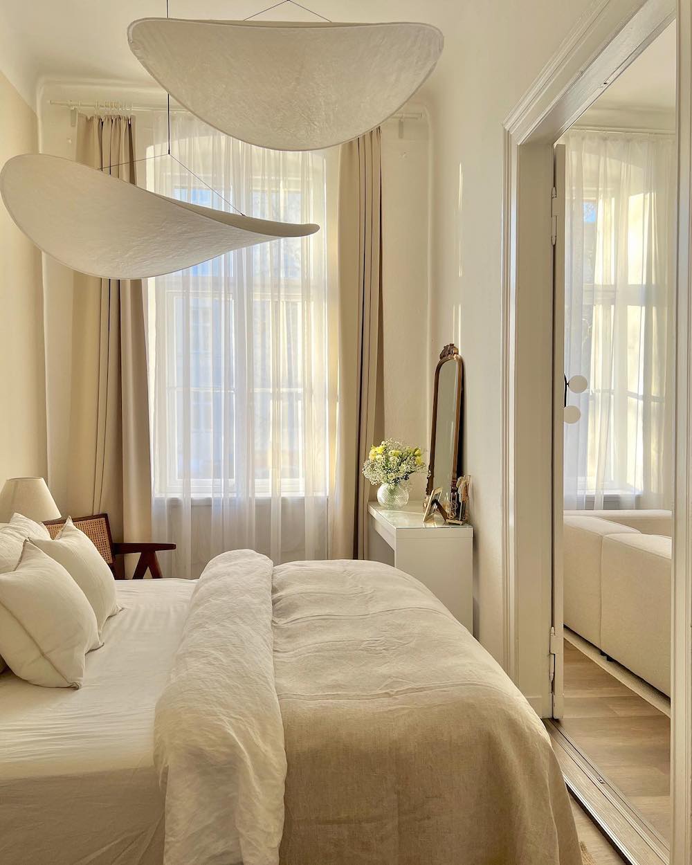 a bedroom with cream bedding and walls with statement ceiling hangings and feminine touches