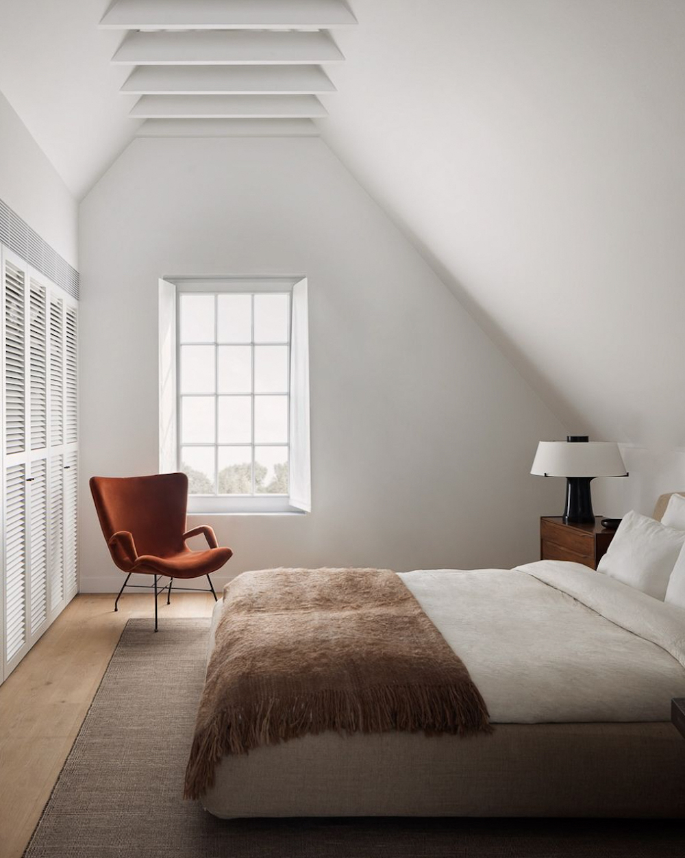 a white minimalist bedroom with cocoa tones and a red reading chair