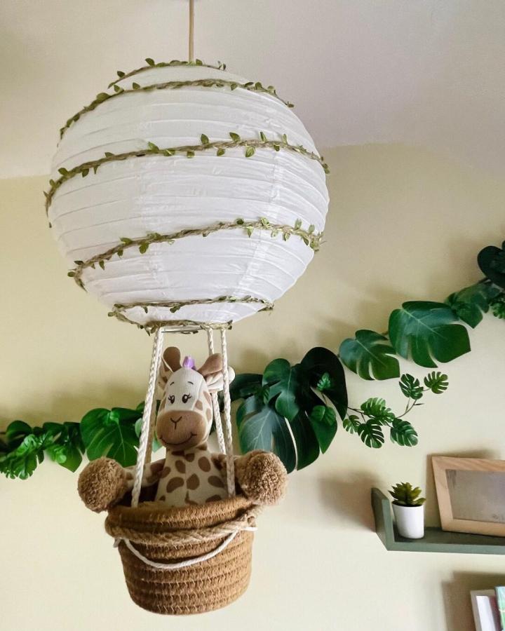 White paper lantern hot air balloon mobile from LunabellCraftByJenna. Features greenery vines and woven basket with giraffe.