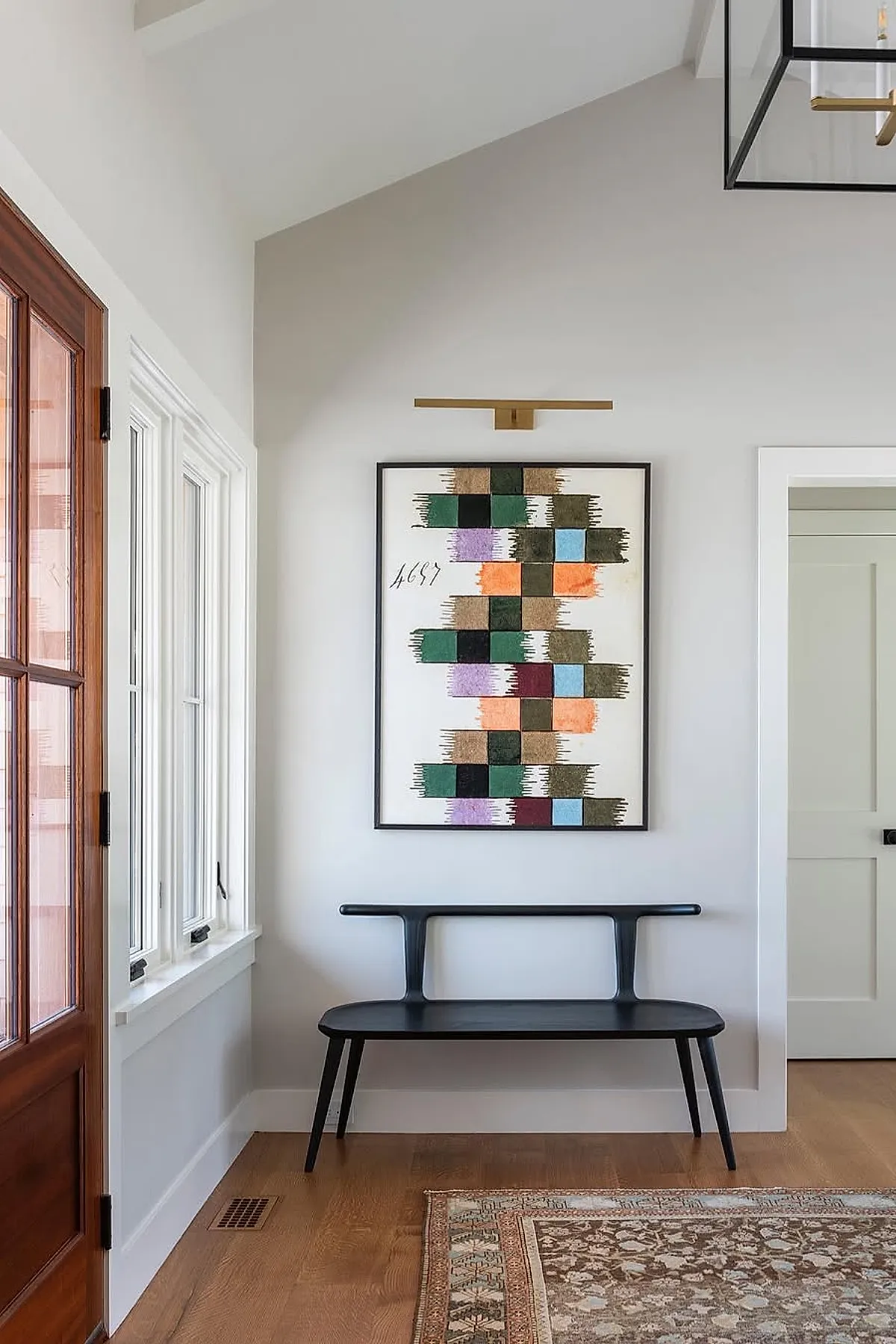 Modern entryway featuring a black bench and colorful geometric artwork on the wall.